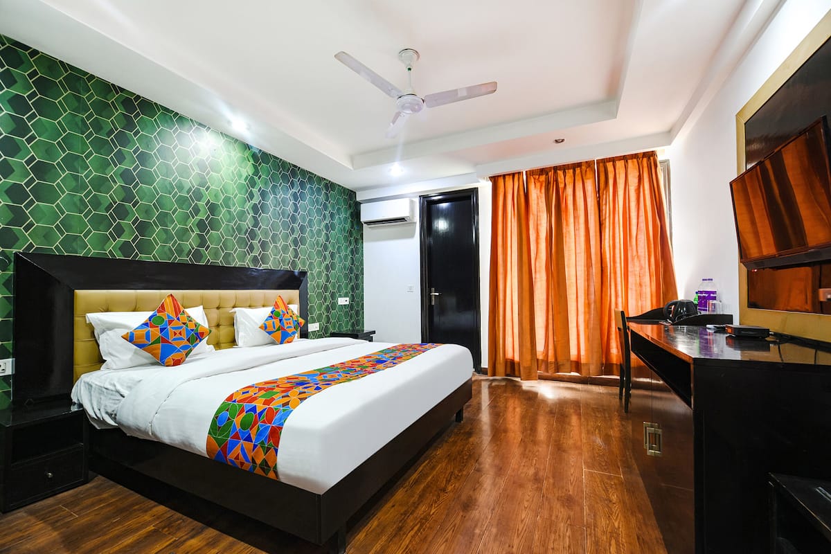 A hotel room with a bed, a desk, a ceiling fan, and a TV.