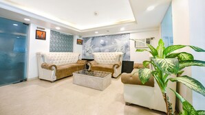 A modern lobby with two beige sofas, a glass coffee table, and a large potted plant. - Fabhotel Cordial Home (New Delhi)