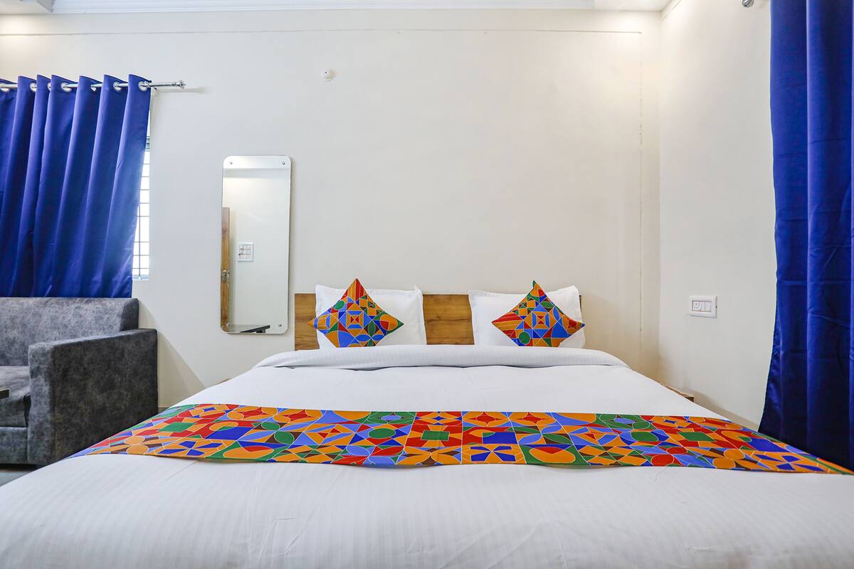 Una habitación de hotel con una cama, una silla, un espejo y cortinas azules.