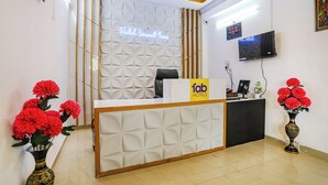 A hotel reception desk with a neon sign, a TV, and two vases with red flowers. - Fabhotel Sonnet Inns (Ranchi)