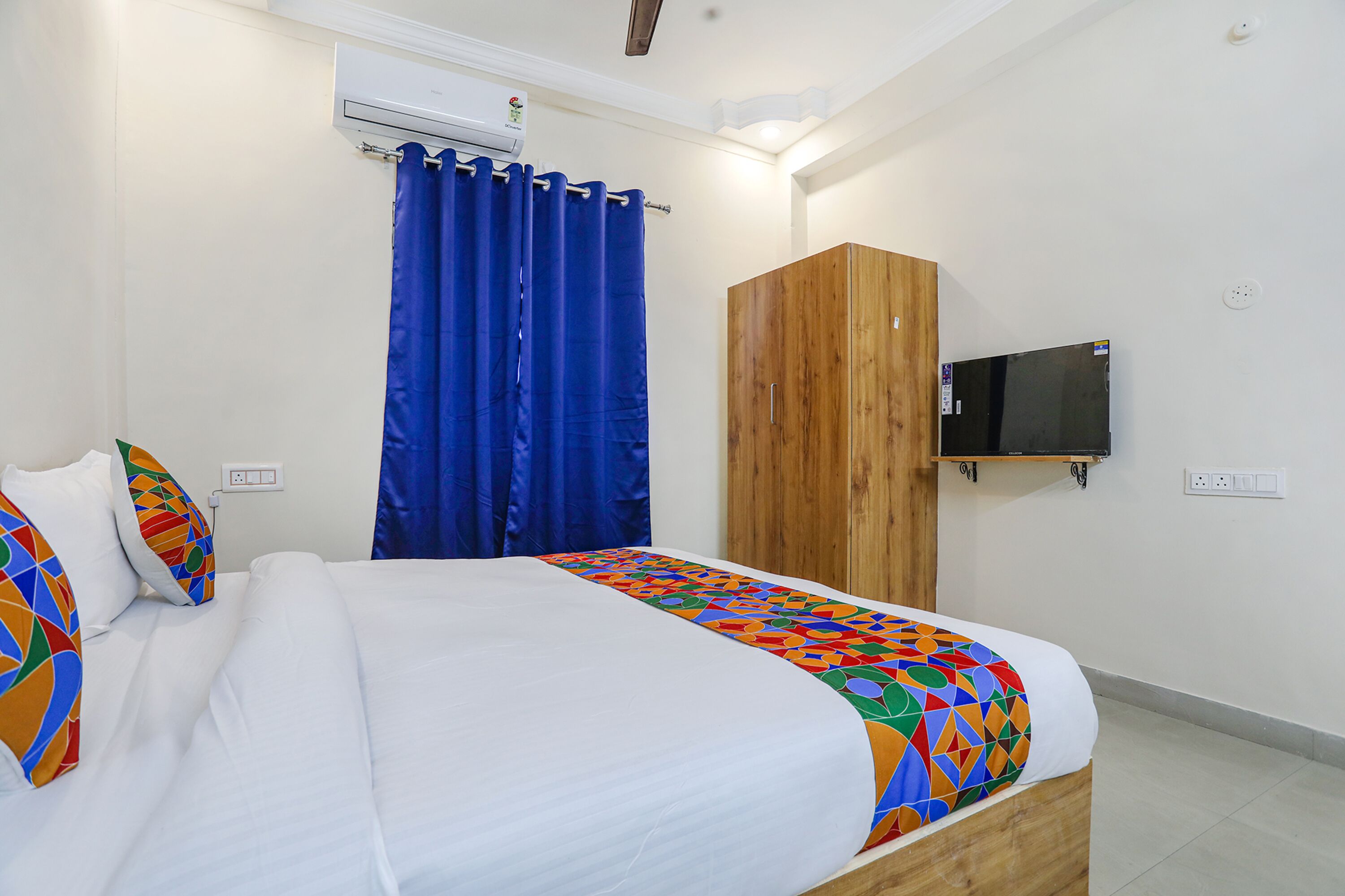 Une chambre à coucher avec un lit, une armoire en bois, un tél éviseur fixé au mur et un rideau bleu.
