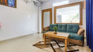 A living room with a sofa, a coffee table, a fan, a window, and a mirror. - Fabhotel Sonnet Inns (Ranchi)