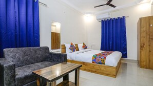 A bedroom with a bed, a wooden wardrobe, a grey sofa, and a small table. - Fabhotel Sonnet Inns (Ranchi)