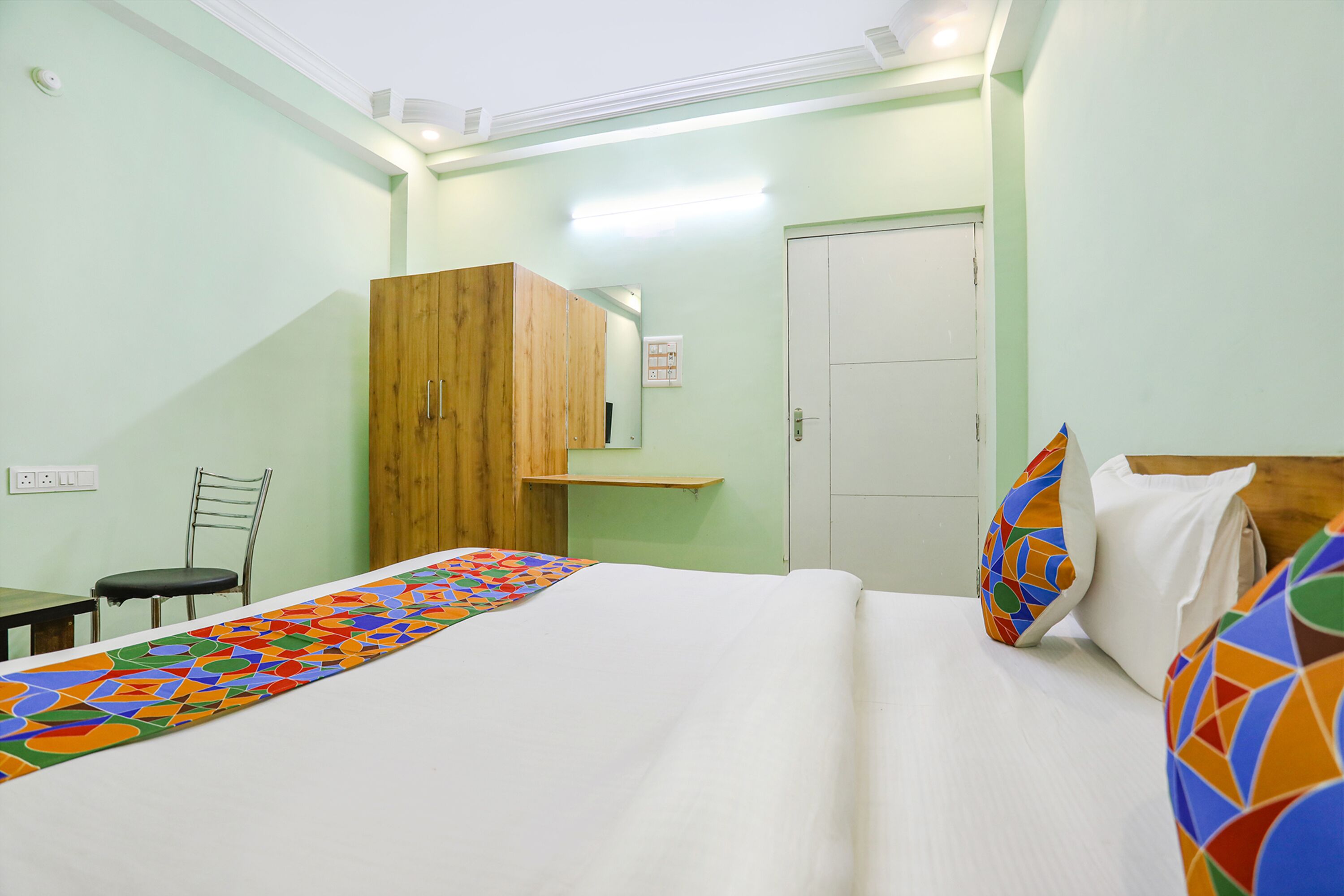 A hotel room with a bed, a wooden wardrobe, a chair, and a small table.
