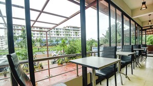 Un restaurante con amplios ventanales, sillas de cuero negro y vistas a un paisaje urbano y áreas verdes.