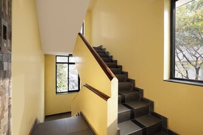 A staircase with a wooden handrail, a small window with a view of the street, and a stone wall on the left. - FabHotel Dewa - Nr. Dabolim International Airport (Sancoale)