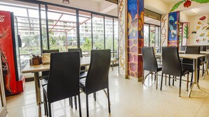 Un comedor con mesas y sillas, ventanas amplias y un mural en la pared.