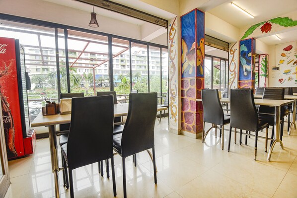 A dining area with tables and chairs, large windows, and a mural on the wall. - FabHotel Dewa - Nr. Dabolim International Airport (Sancoale)