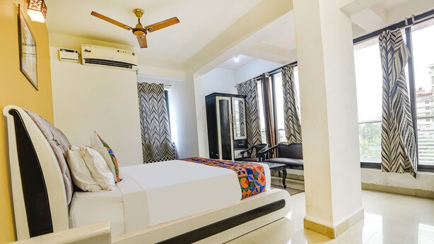 Habitación de hotel con cama, aire acondicionado, ventilador de techo y vistas al exterior a través de amplios ventanales.