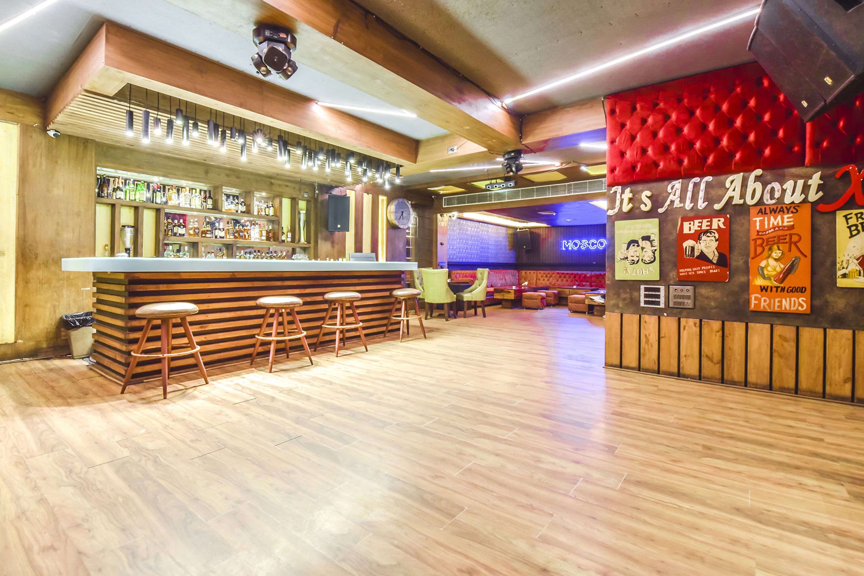 A bar area with wooden flooring, bar stools, and a counter with bottles.