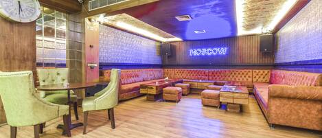 Eine Lounge mit einer Uhr, Holzboden und einem Neonlichtschild mit der Aufschrift 'MOSCPW'.