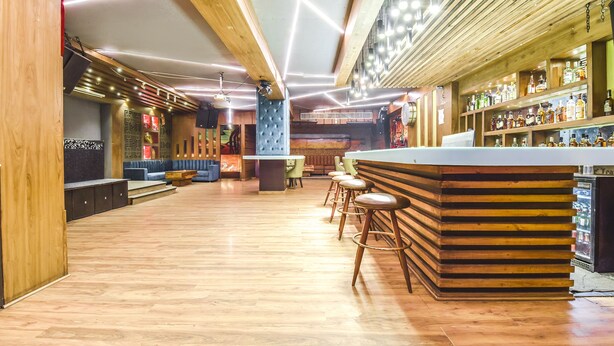 A bar area with wooden flooring, a counter with stools, and shelves with bottles. - Fabhotel Four Boutique (Jaipur)