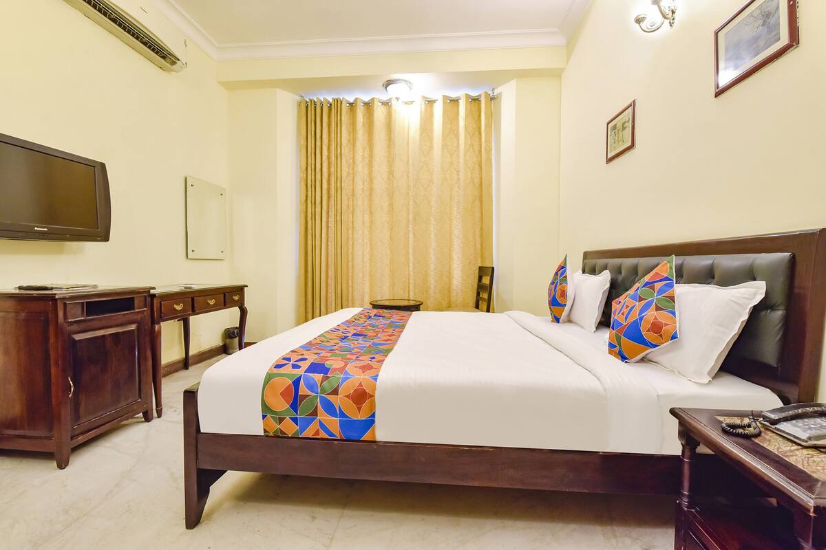 A hotel room with a large bed, a wooden desk, a television, and a curtain.