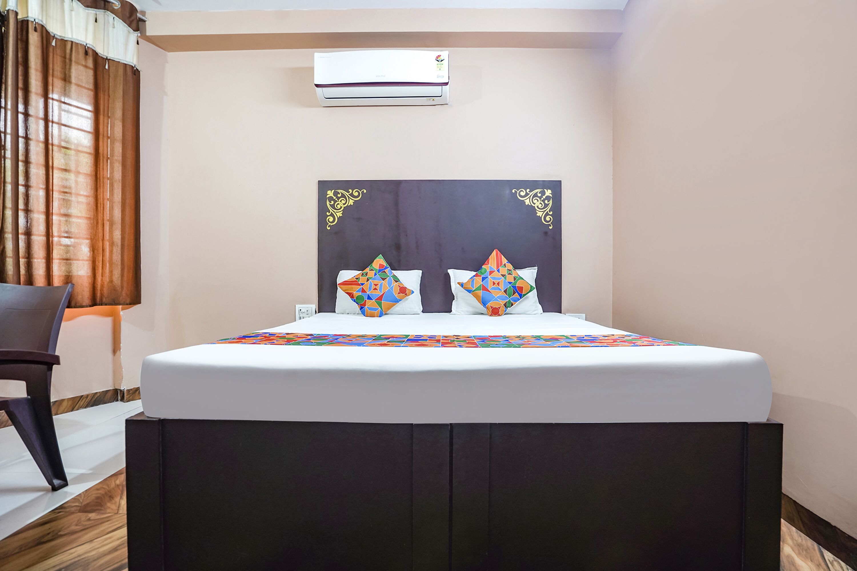Un lit bien fait, avec une couvre-lit à motifs, une tête de lit sombre et deux coussins décoratifs.