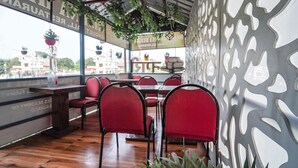 A restaurant with red chairs and tables, a decorative wall, and hanging plants. - Fabhotel Krishna Heights (Dehradun)