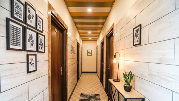 A hallway with framed botanical prints on the walls, a checkered rug, and a table with a potted plant. - Fabhotel Krishna Heights (Dehradun)