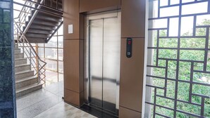 An elevator with a digital display, a staircase with metal railings, and a view of greenery outside. - Fabhotel Krishna Heights (Dehradun)