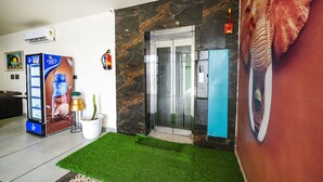 A lobby with a glass elevator, a potted plant, a Cream Bell advertisement, and a large elephant mural.