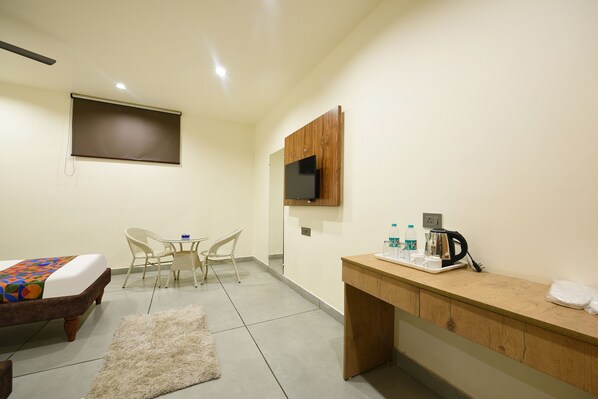 A hotel room with a bed, a desk with a coffee maker, a TV, and a small table with chairs. - Fabhotel Bleu Ville (Faridabad)