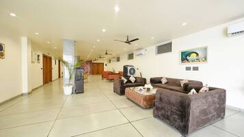 A spacious lobby with a high ceiling, multiple ceiling fans, and a large seating area with sofas and a coffee table.