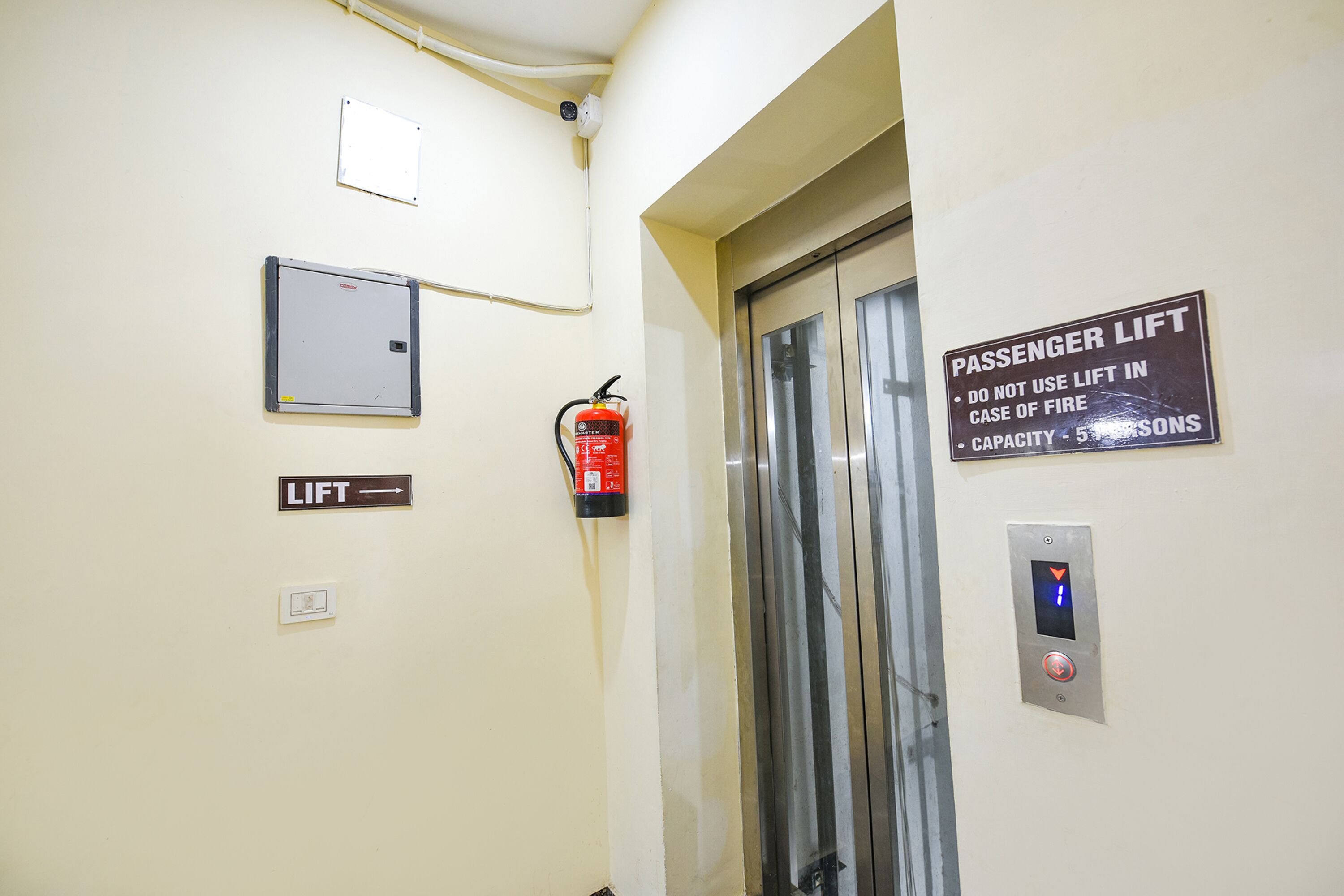 Un ascenseur portant une signalisation indiquant une capacité maximale de cinq personnes et un avertissement interdisant son utilisation en cas d’incendie.