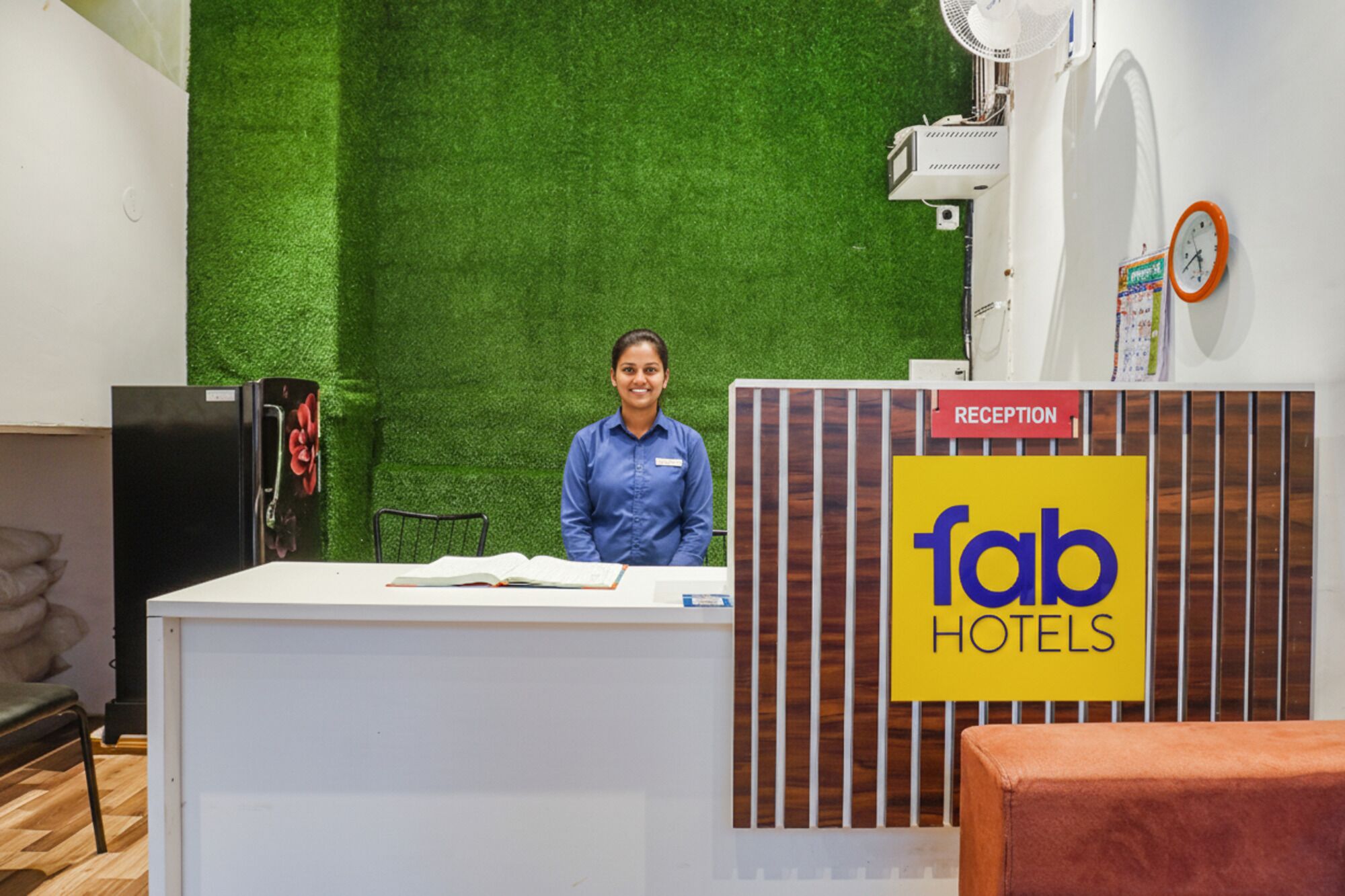 A reception desk with a green artificial grass backdrop, a clock, and a sign for 'fab hotels'.