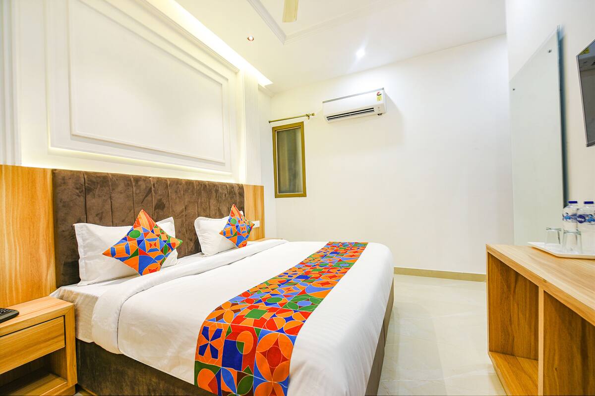 A hotel room with a large bed, a wooden headboard, a bedside table, a nightstand, a desk, and a mirror.