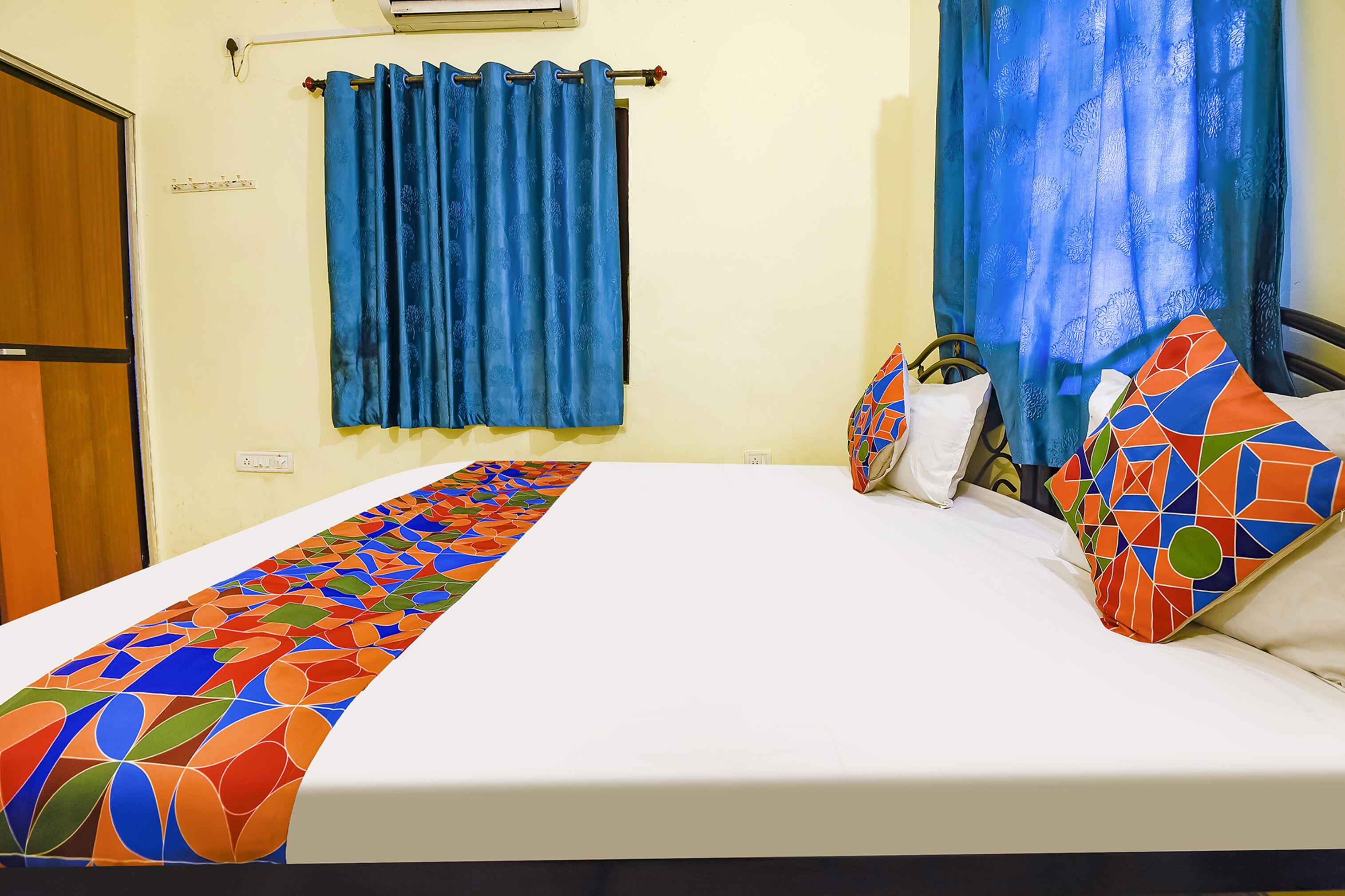 A hotel room with a bed, a curtain, and a wall socket.