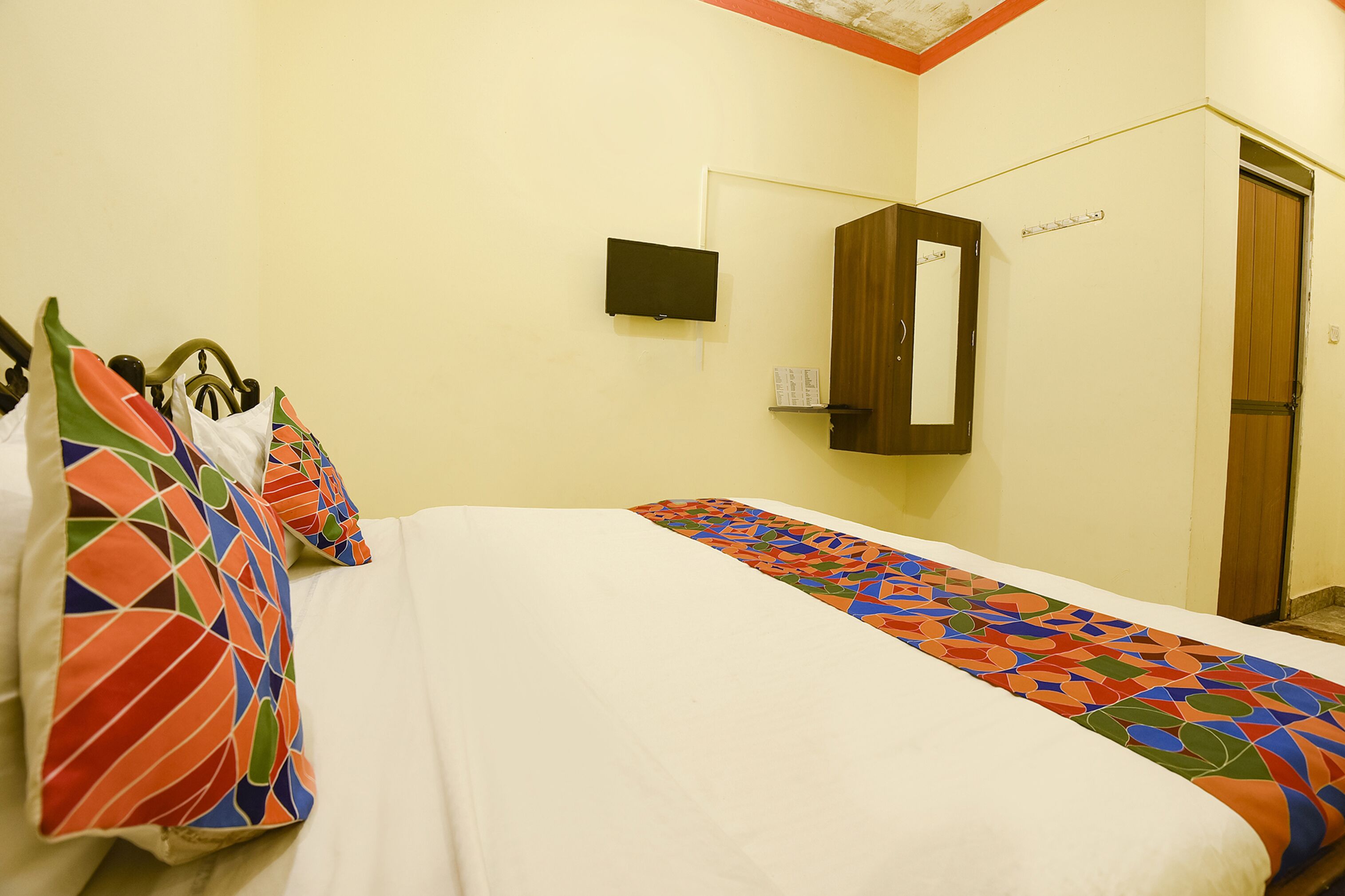 A hotel room with a bed, a TV, a mirror, and a door.