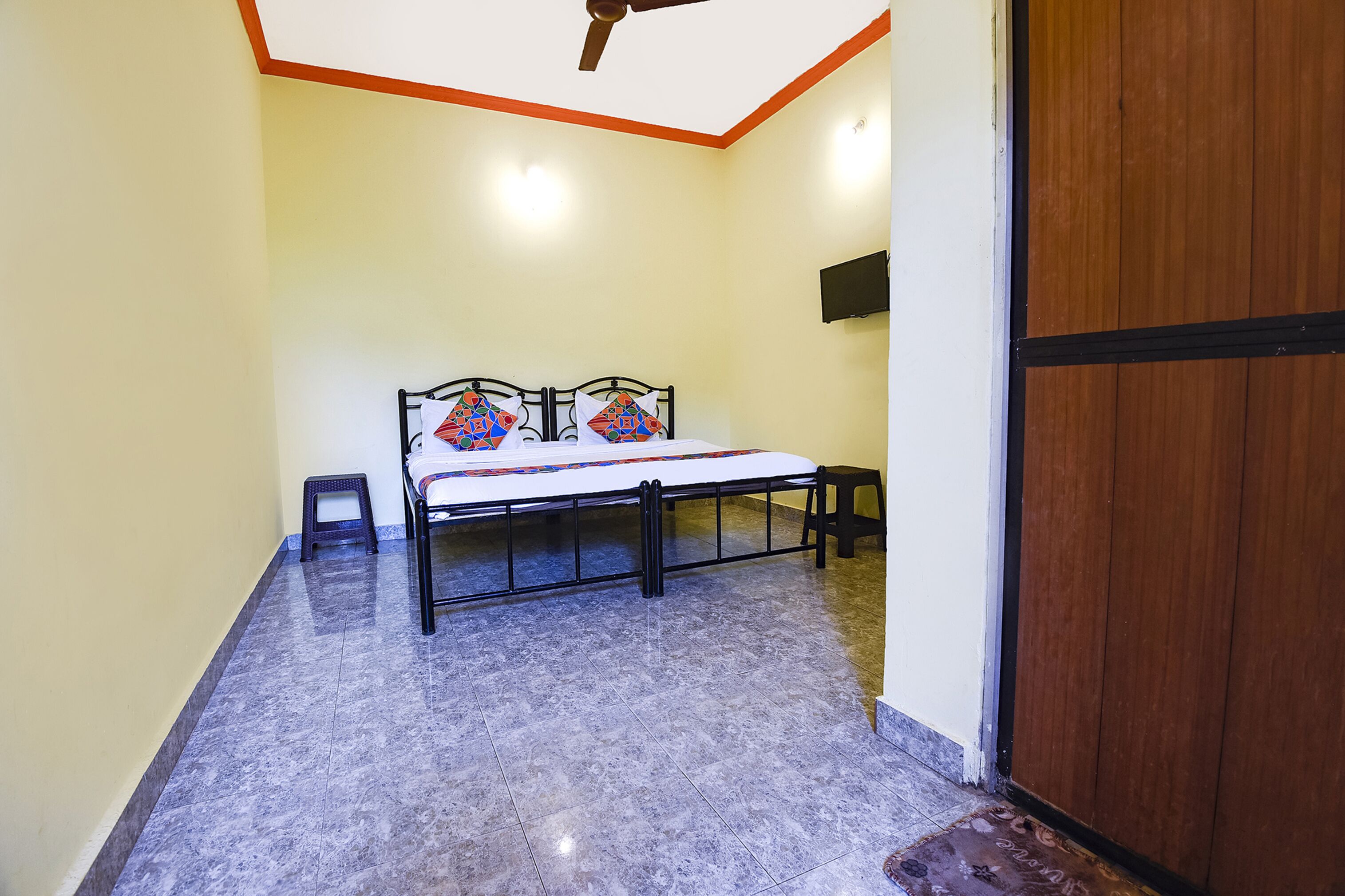 A room with a bed, a ceiling fan, a TV mounted on the wall, and a wooden door.
