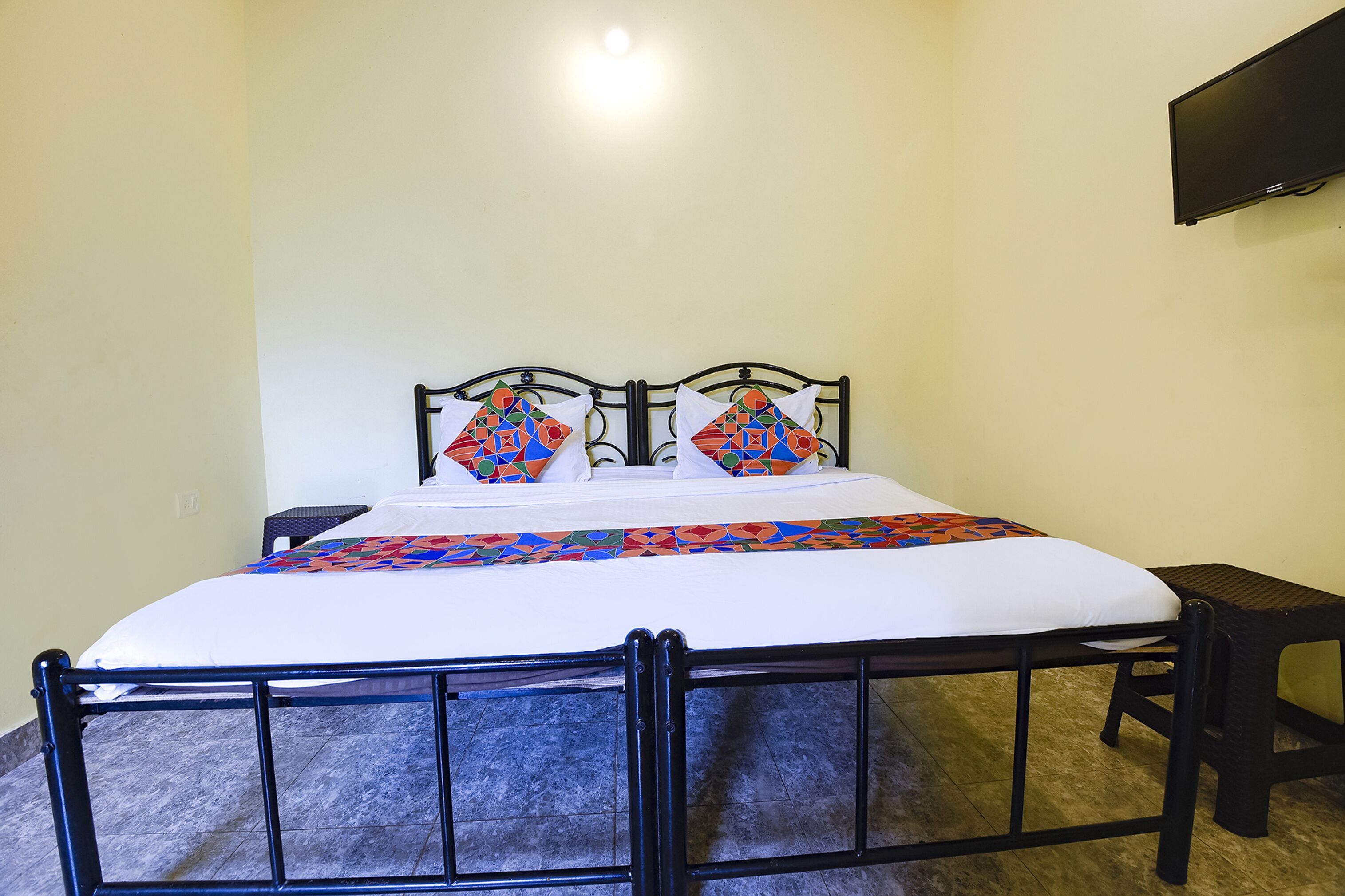 A single bed with a black metal frame, white bedding, and colorful geometric pillows.