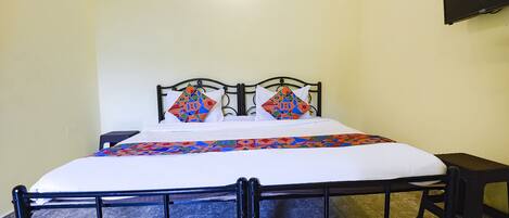 A single bed with a black metal frame, white bedding, and colorful geometric pillows.