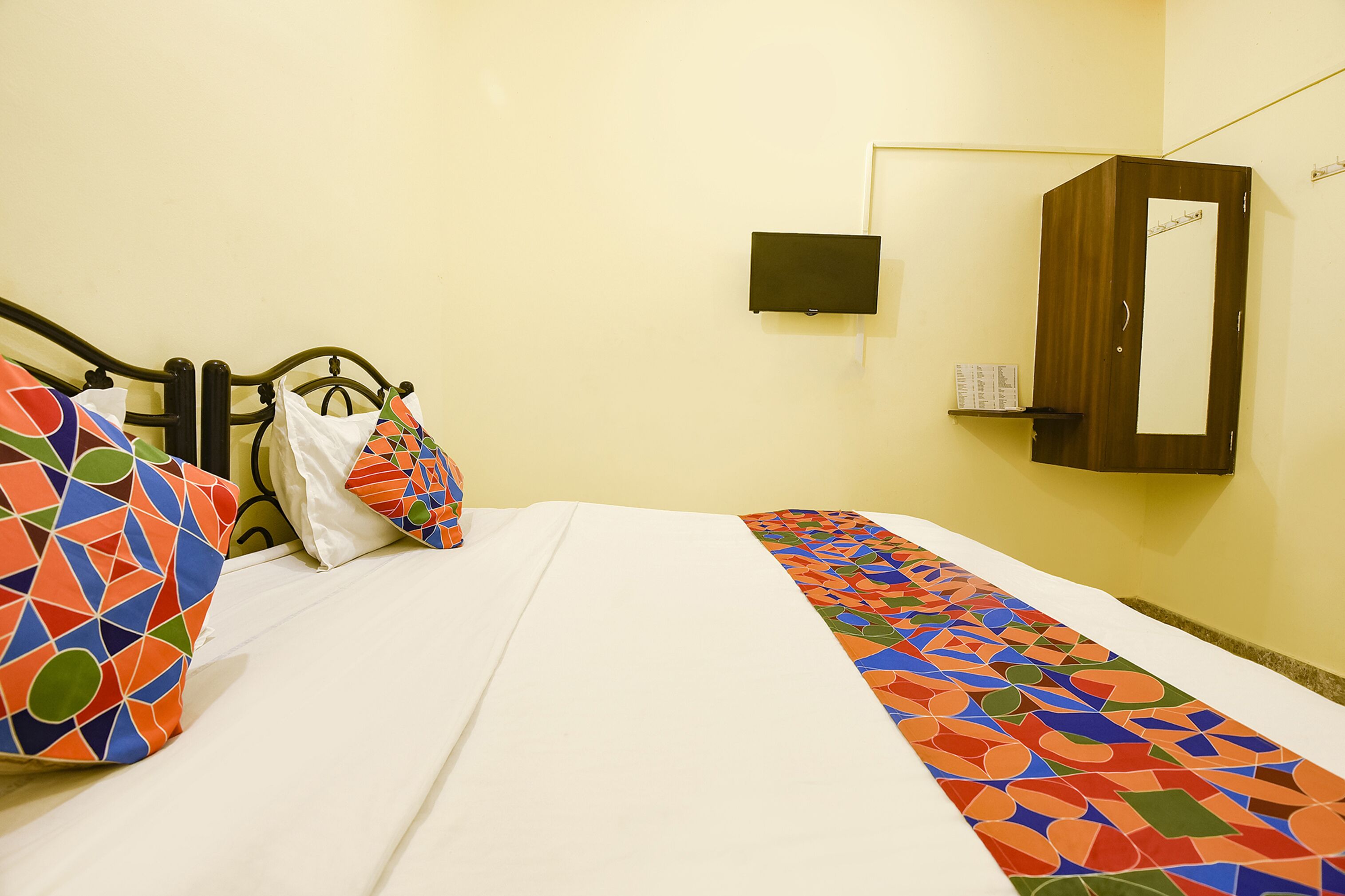 A hotel room with a bed, pillows, a small table, and a mirror.