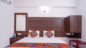 Una habitación de hotel con una cama grande, un cabecero de madera, una mesita de noche, un tocador, un espejo y un armario.