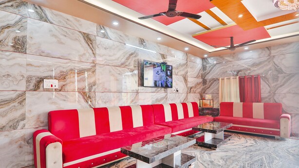 Una hall moderna con pareti in marmo, un divano rosso e bianco, ventilatori a soffitto e un televisore a parete.