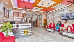 Una hall d'albergo con reception, divani rossi, pavimento in marmo, ventilatori a soffitto e uno schermo televisivo.