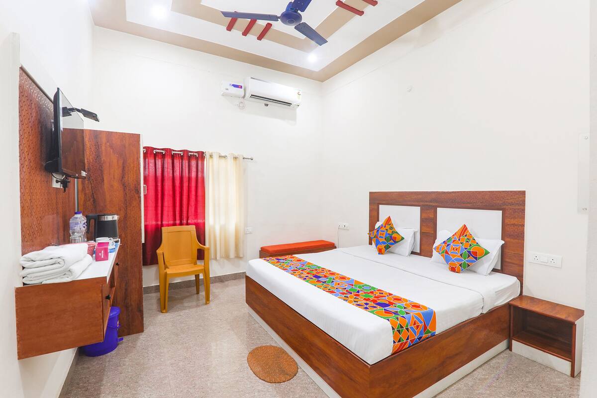 A hotel room with a wooden bed, a desk with a chair, a television, and an air conditioning unit.