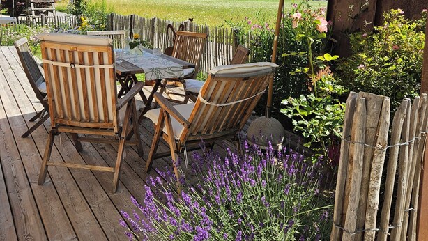 An outdoor patio with wooden furniture, a large umbrella, and a view of mountains and a church.