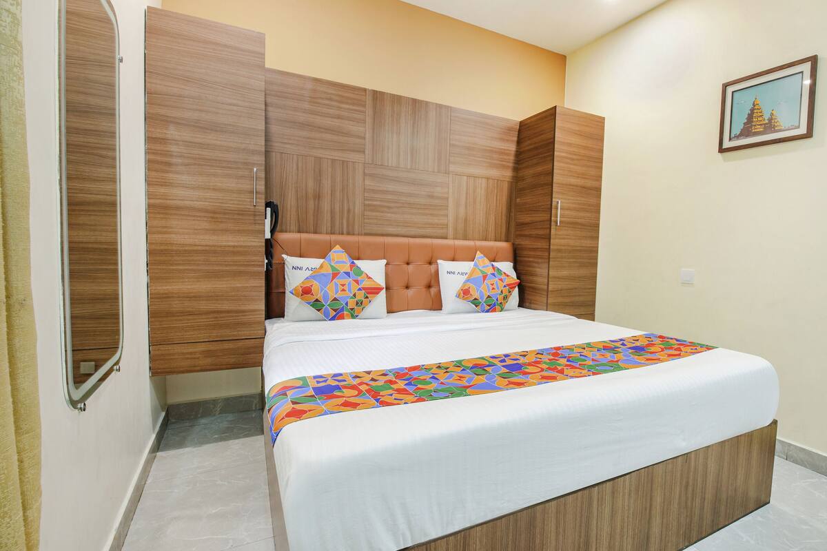 Ein Hotelzimmer mit einem Bett, einem Holzkopfende, zwei Kissen, einer farbenfrohen Tagesdecke und einem gerahmten Bild an der Wand.