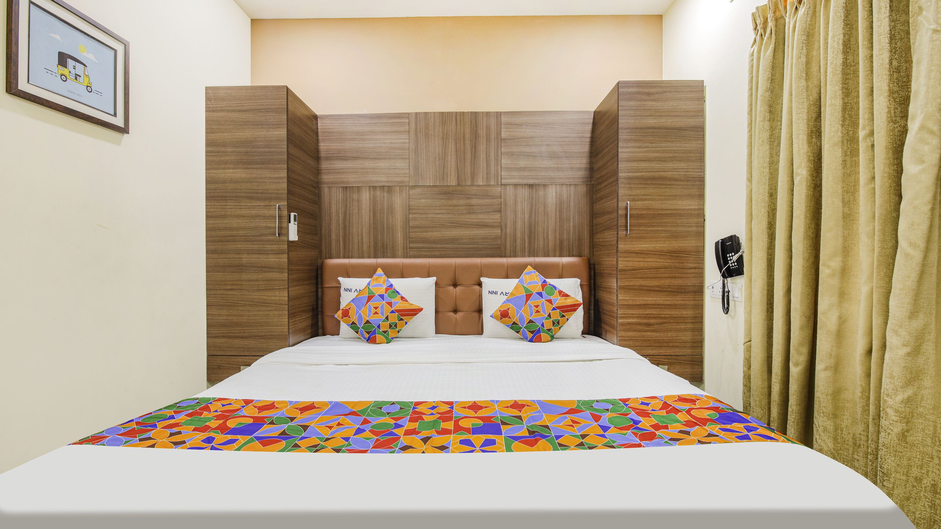 A neatly made bed with a colorful geometric-patterned bedspread, a brown upholstered headboard, and two decorative pillows with a similar pattern.