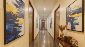 Un couloir aux murs ornés de peintures abstraites, doté d’un plancher ciré et agrémenté d’un banc en bois sur lequel sont disposés des objets décoratifs.