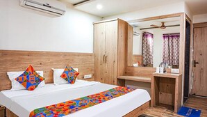 Una habitación de hotel con cama, armario de madera, espejo y un escritorio pequeño.