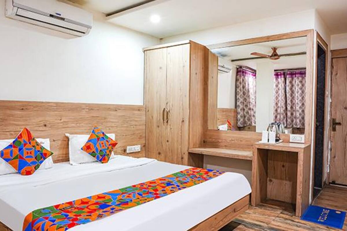 A hotel room with a bed, a wooden wardrobe, a mirror, and a small desk.