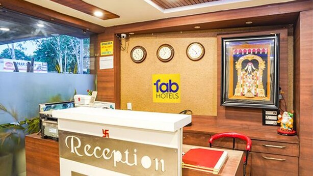 Una mesa de recepción con un letrero que dice "Reception" y el logotipo de "fab hotels". Hay tres relojes en la pared y una imagen religiosa enmarcada.