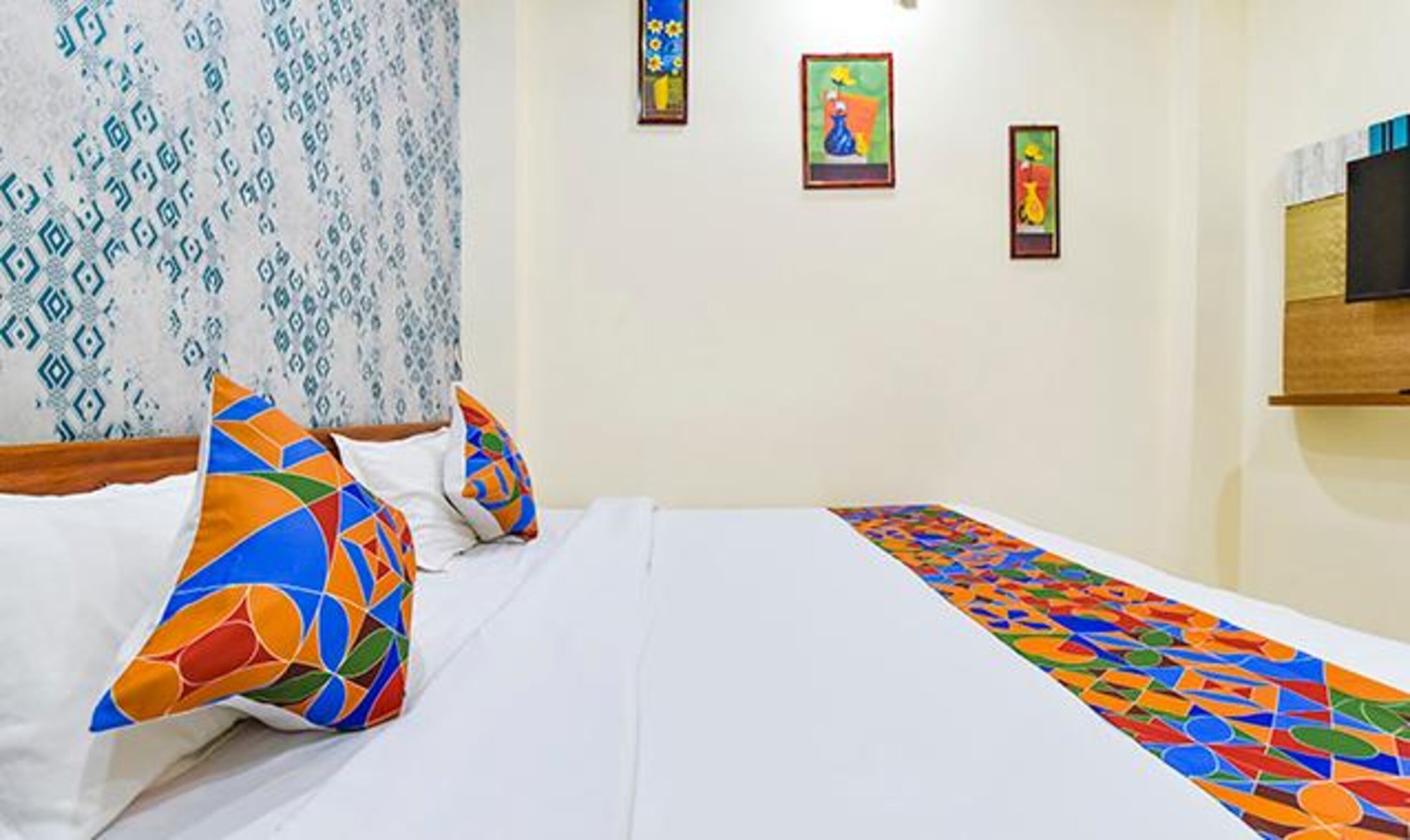 Una camera d'albergo con un letto rifatto, cuscini colorati e una parete decorata.