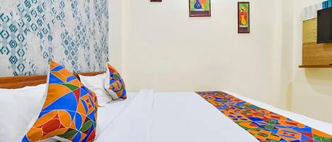 A hotel room with a neatly made bed, colorful pillows, and a patterned wall.