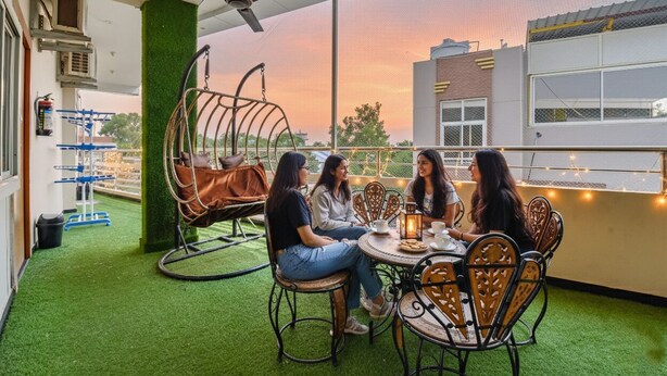 Una terraza en la azotea con una mesa redonda y sillas, un sillón colgante y vistas al atardecer.