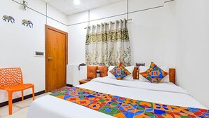 Una habitación de hotel con cama, almohadas, una silla y un ventanal con cortinas.