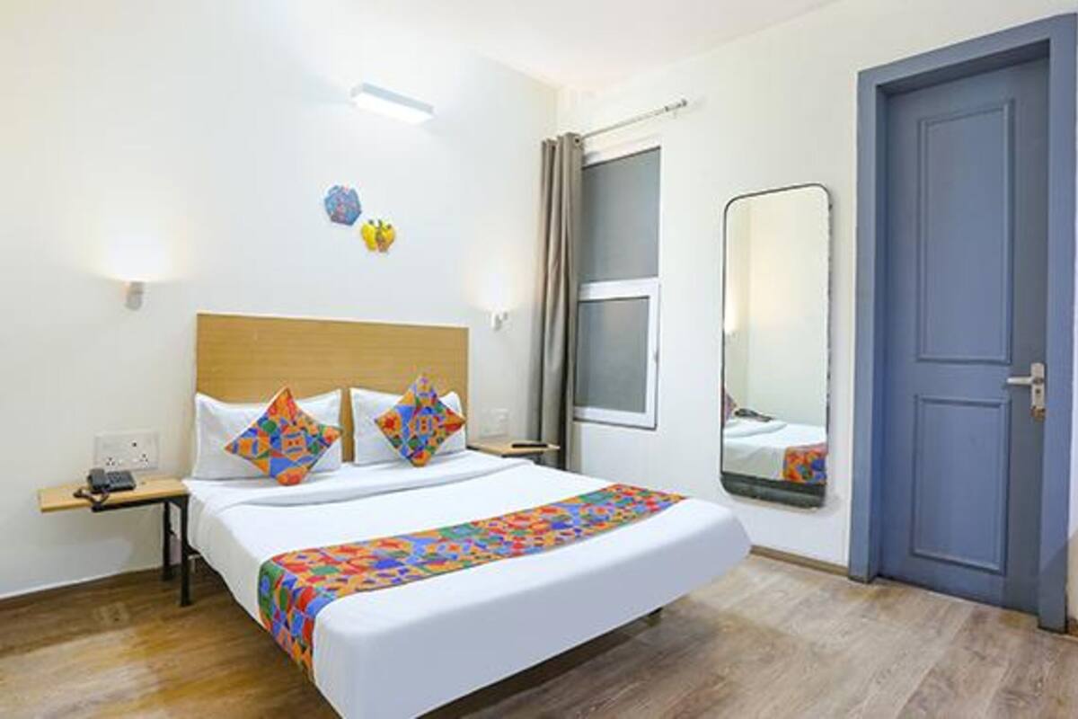 A hotel room with a bed, a bedside table, a mirror, and a door.