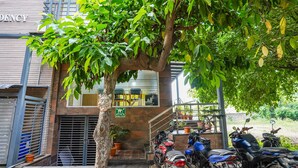 Un edificio con un letrero que dice "DENCY" y un árbol en la parte delantera. Hay motocicletas estacionadas afuera.